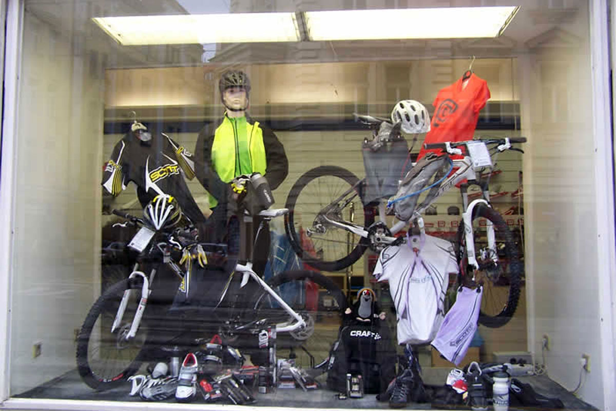 Prodejna sportovních potřeb, část pro cyklistiku, naaranžovaná výloha s nabídkou vybavení pro cyklisty