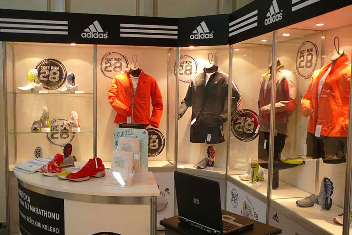 Vitríny a stolek na výstavní expozici s produkty Adidas, límce stánku vylepené logy Adidas
