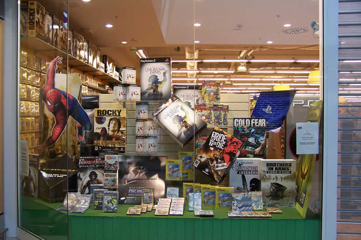 Výloha prodejny s videohrami, naaranžované makety, krabice a nosiče CD, DVD a dalších nosičů 