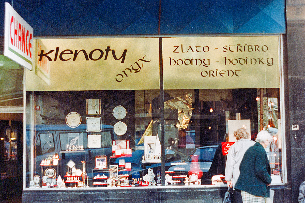 Nápis pekařství na černém skle, zlatý rámeček, červená pečeť, logo a rohlík na výloze